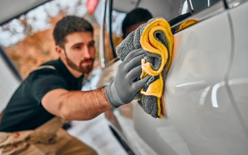 Homme essuyant une voiture blanche avec un chiffon lors d&#039;un nettoyage professionnel.