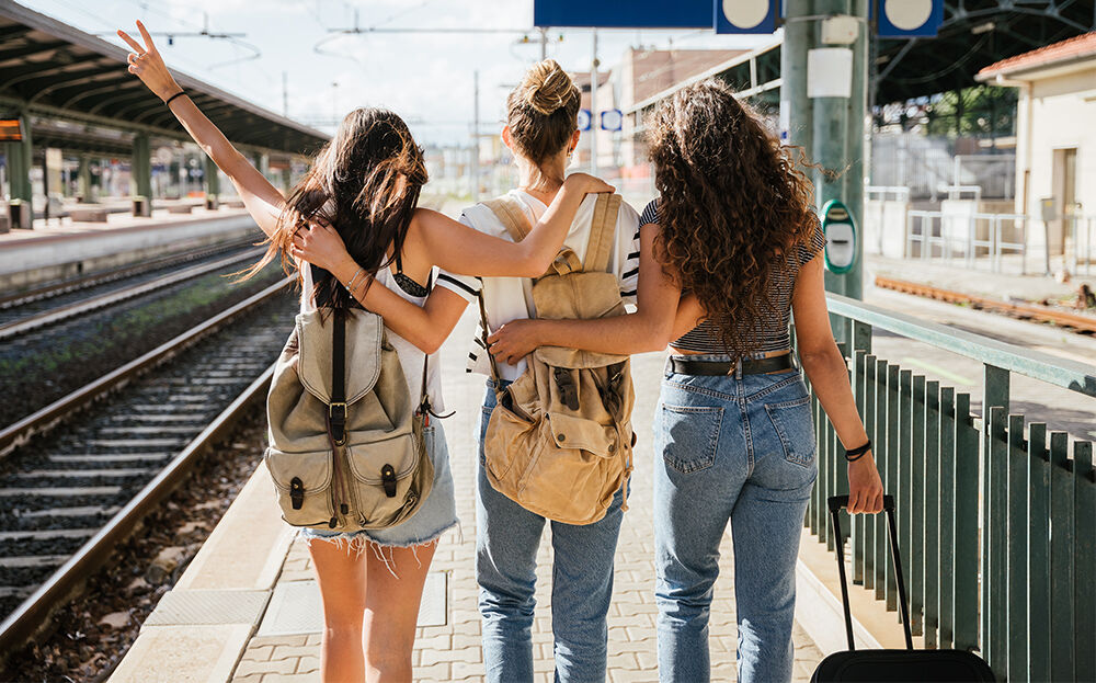 3 Freunde warten gut gelaunt auf dem Perron auf den Zug