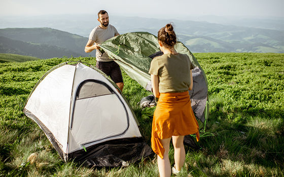 Una coppia monta la tenda su un prato di montagna al di sopra della linea degli alberi.