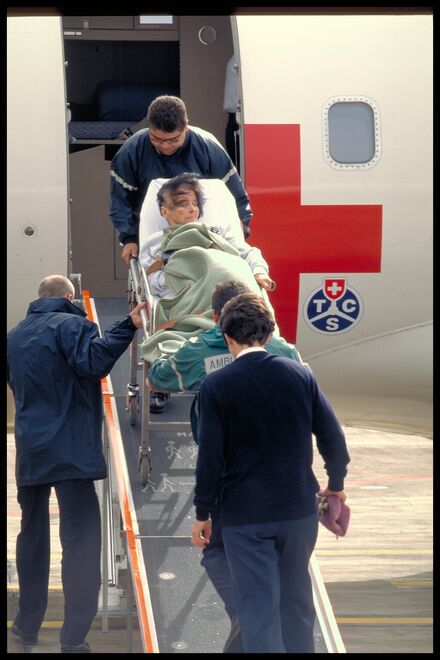 Foto eines Rega-Flugzeugs mit TCS-Logo und Personen, die eine Person auf einer Bahre in das Flugzeug verladen