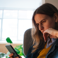 Una donna guarda il proprio smartphone con la fronte aggrottata.