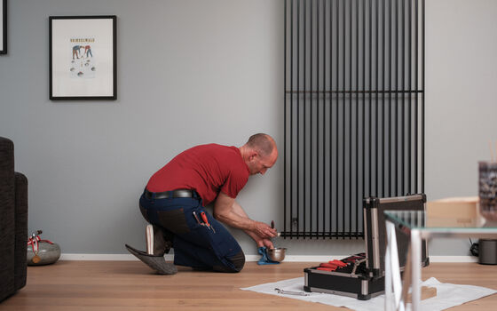 Mann hält kleines Gefäss an Heizungsventil und entlüftet die Heizung.