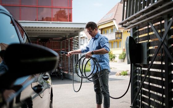 Un homme recharge sa voiture électrique sur sa borne de recharge à domicile.