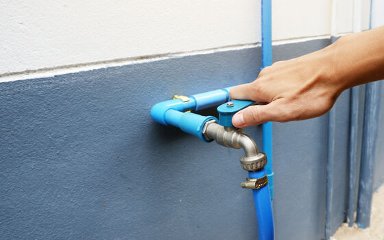 Eine Hand dreht an einem Wasserhahn um die Wasserleitung zu entleeren.